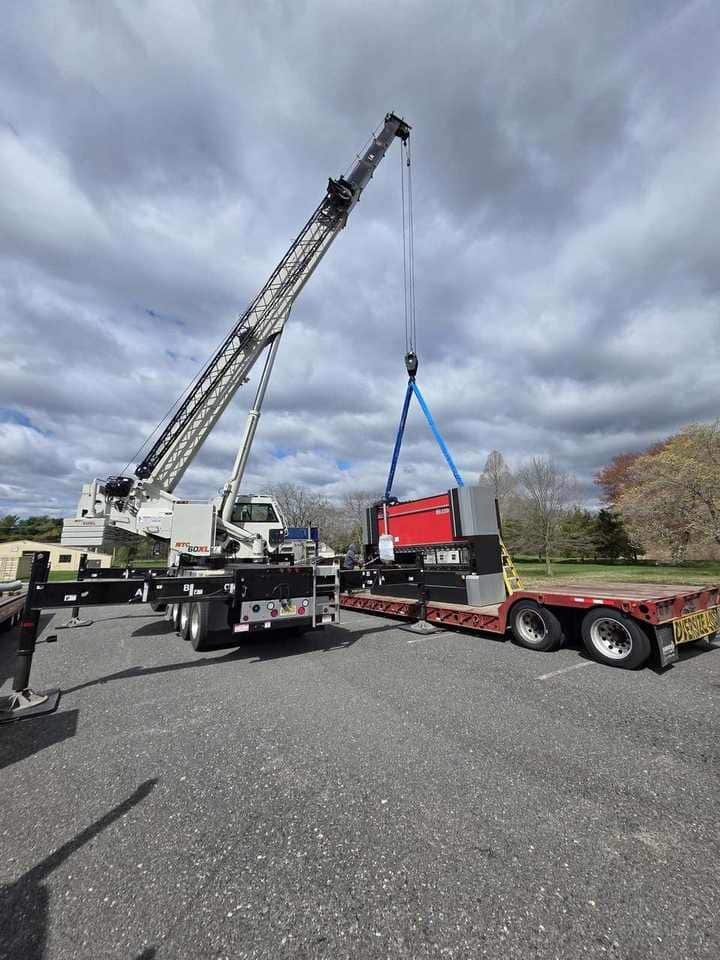 Steedle truck crane lifting industrial machinery from a flatbed trailer into position
