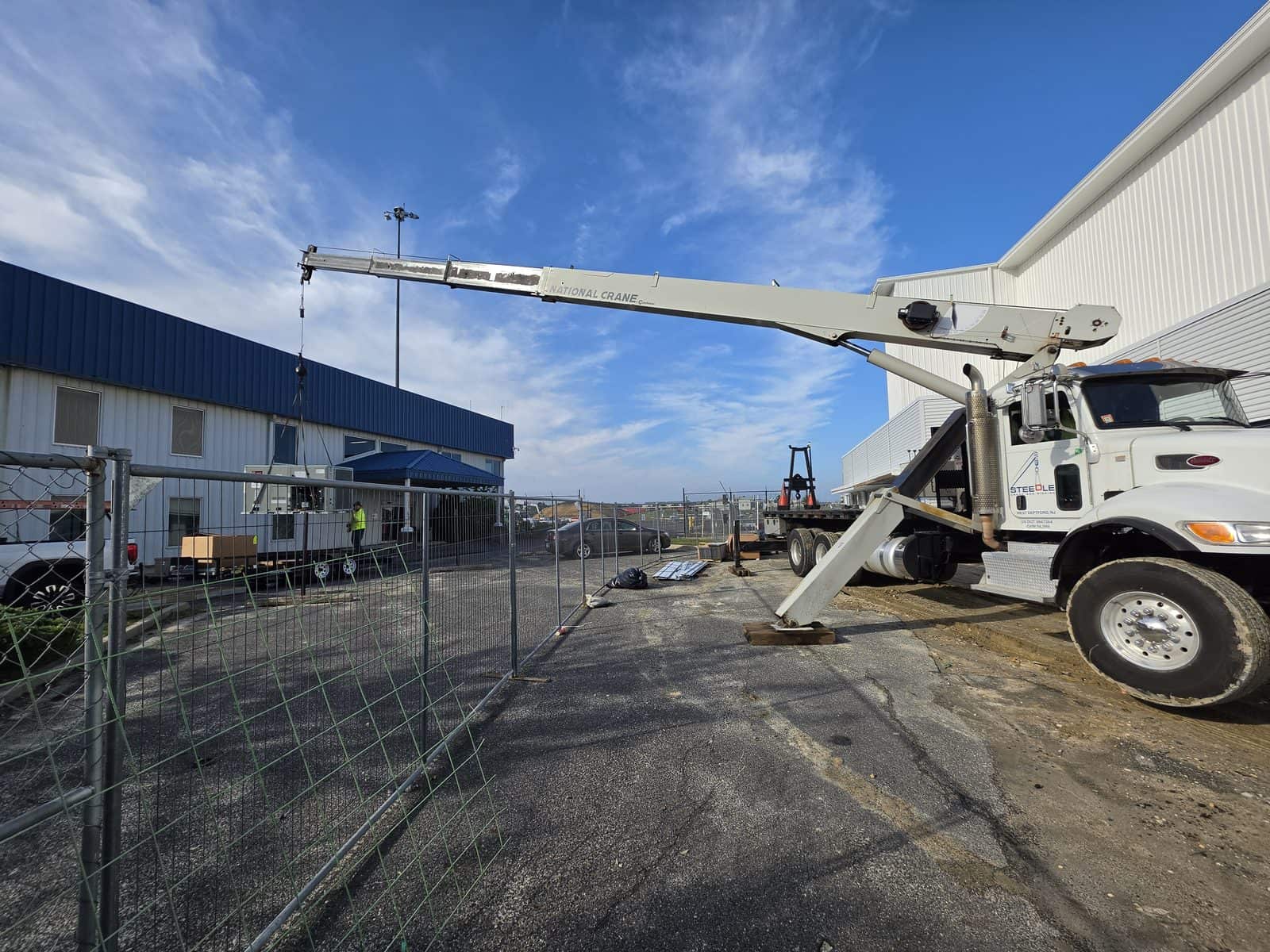 Steedle truck crane with the boom extended low and nearly horizontal over a temporary fence beside a hangar near the Atlantic City airport