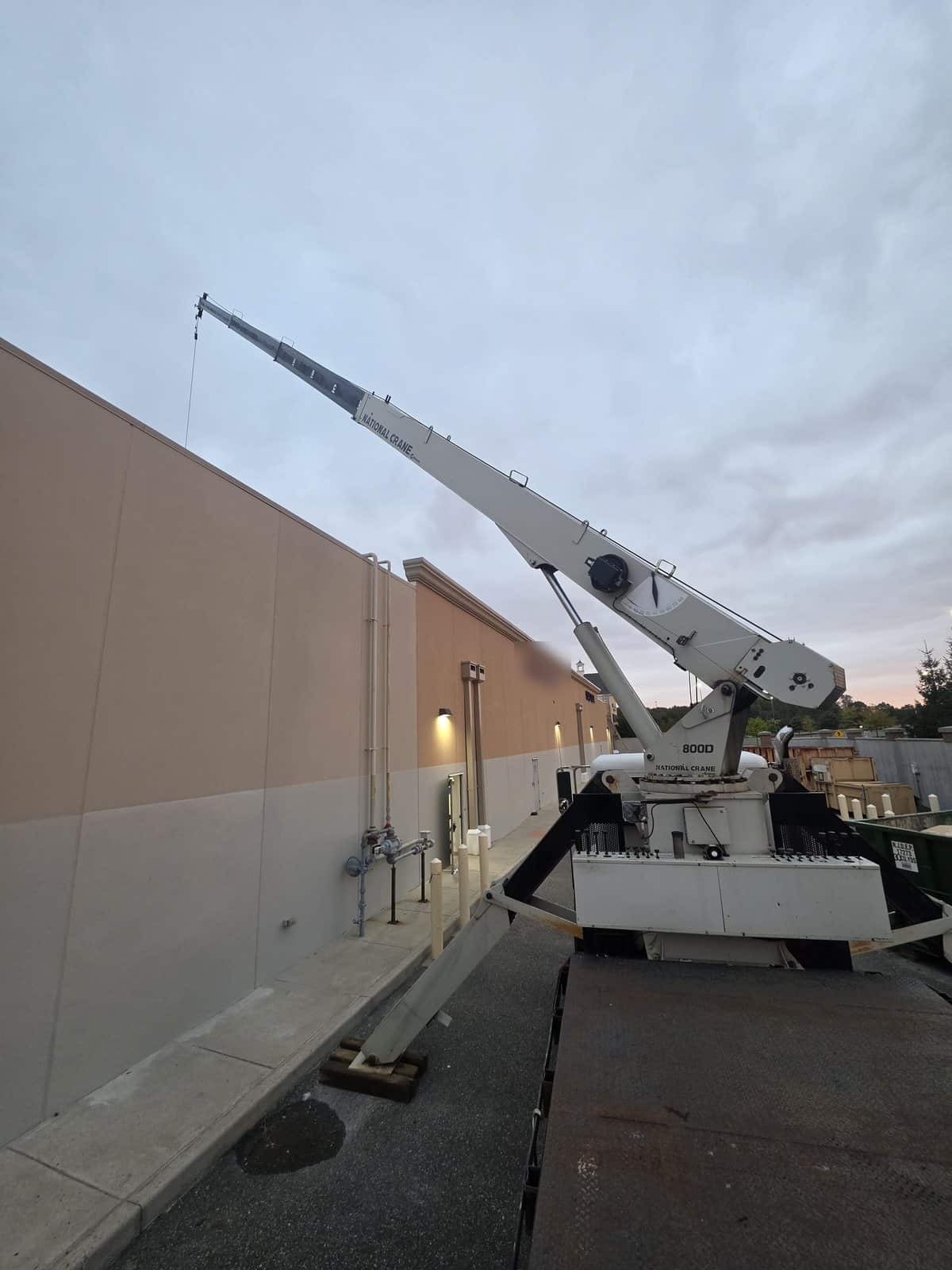 Steedle National Crane 800D on a flatbed with the boom raised along the wall of a retail building in Gloucester Township, NJ at sunrise