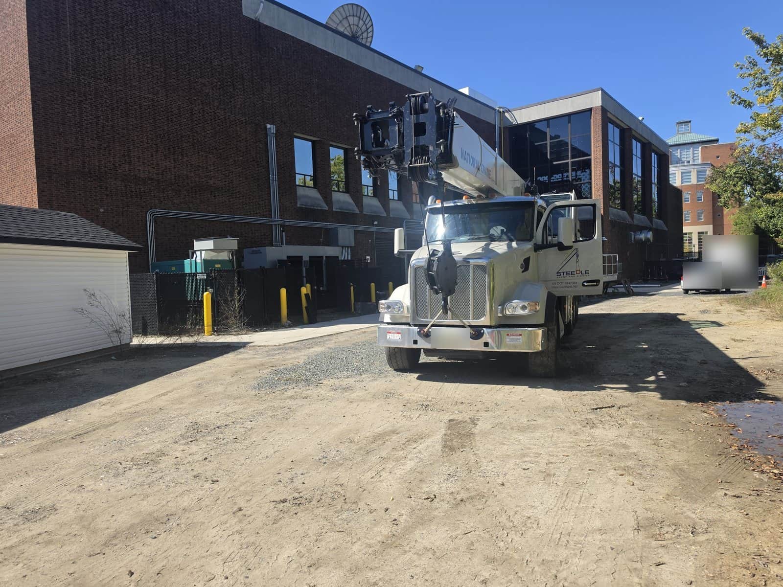 Steedle truck crane arriving on a gravel access lane beside a brick building at a facility in Glassboro, NJ