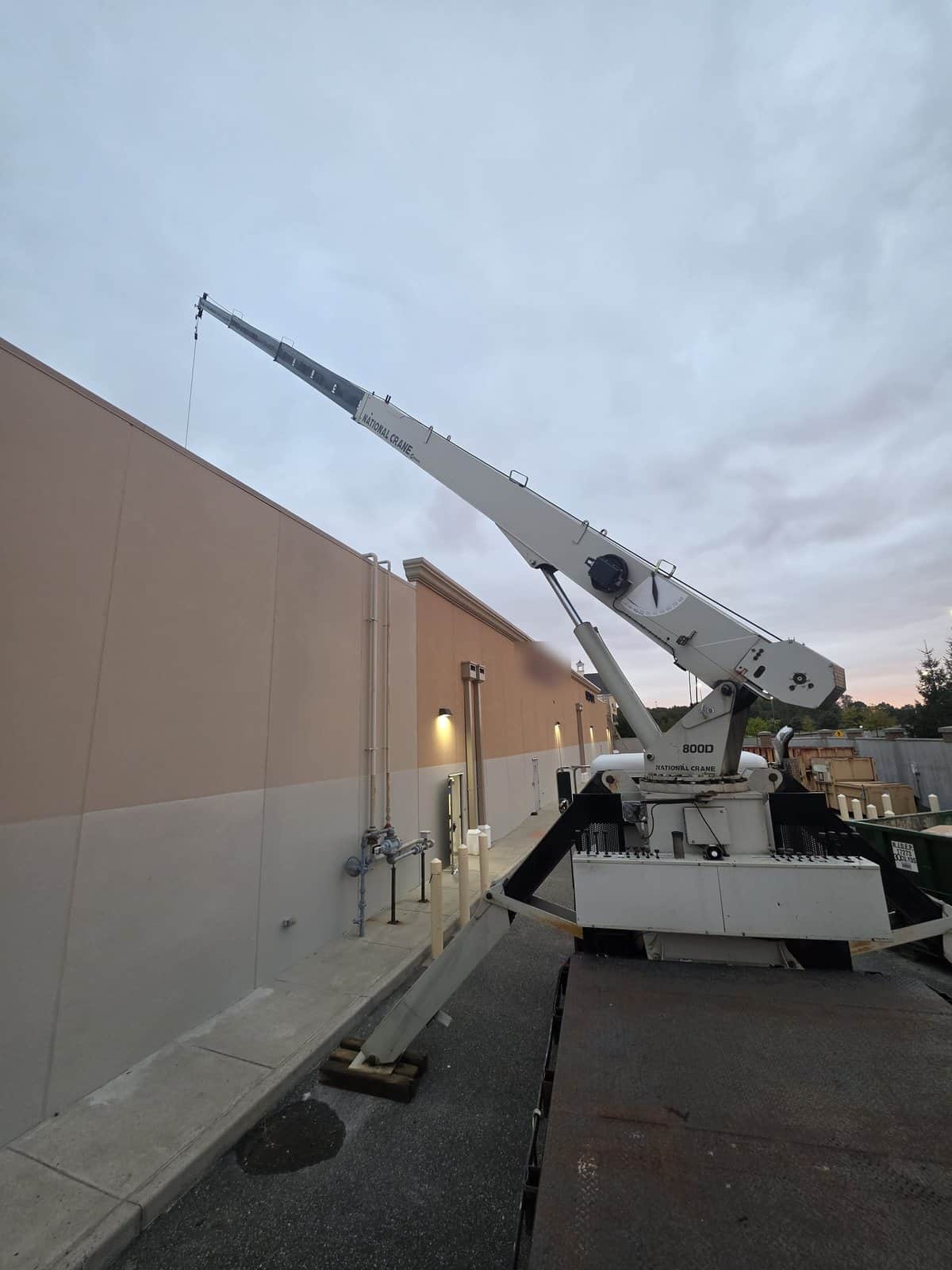 Steedle National Crane 800D on a flatbed with the boom raised along the wall of a retail building in Gloucester Township, NJ at sunrise