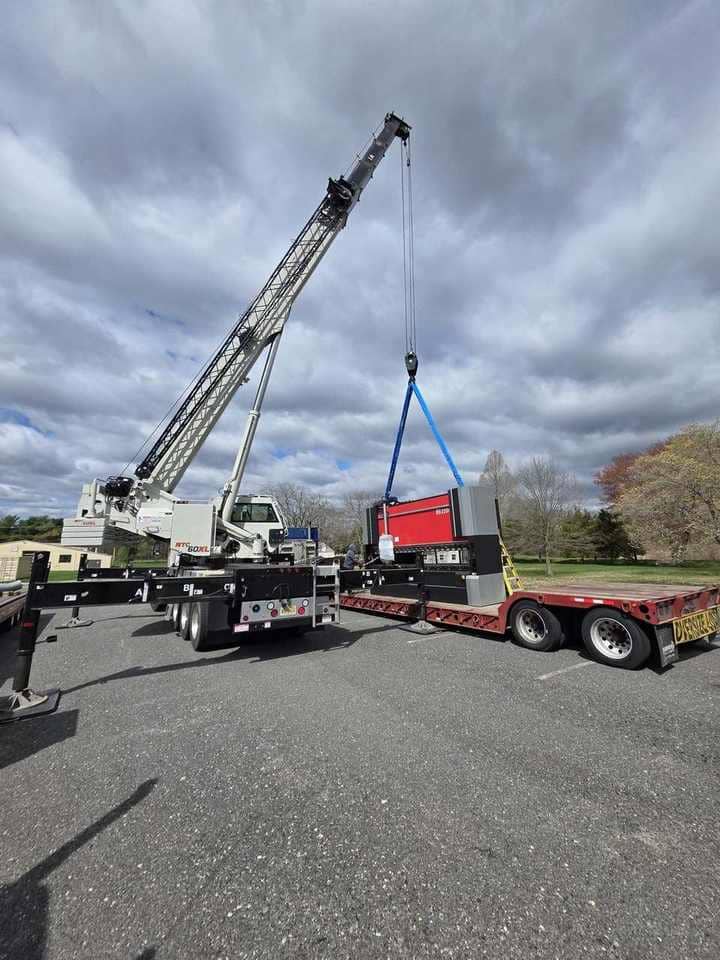 Steedle truck crane lifting industrial machinery from a flatbed trailer into position