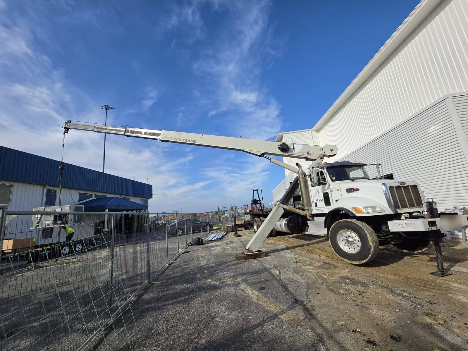 Steedle truck crane on outriggers beside a hangar with a worker in hi-vis at equipment on a trailer near the Atlantic City airport