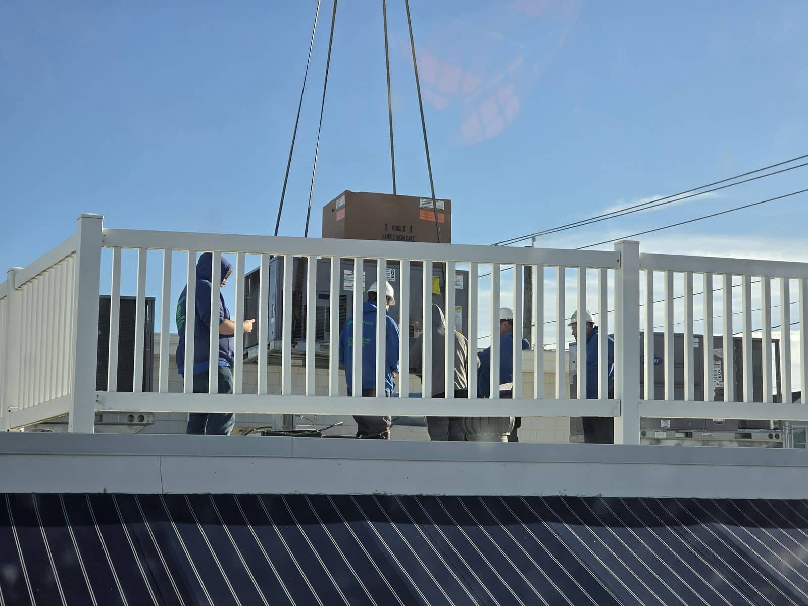 Crew in hard hats on the roof guiding a new rooftop unit into place in Ocean City, NJ