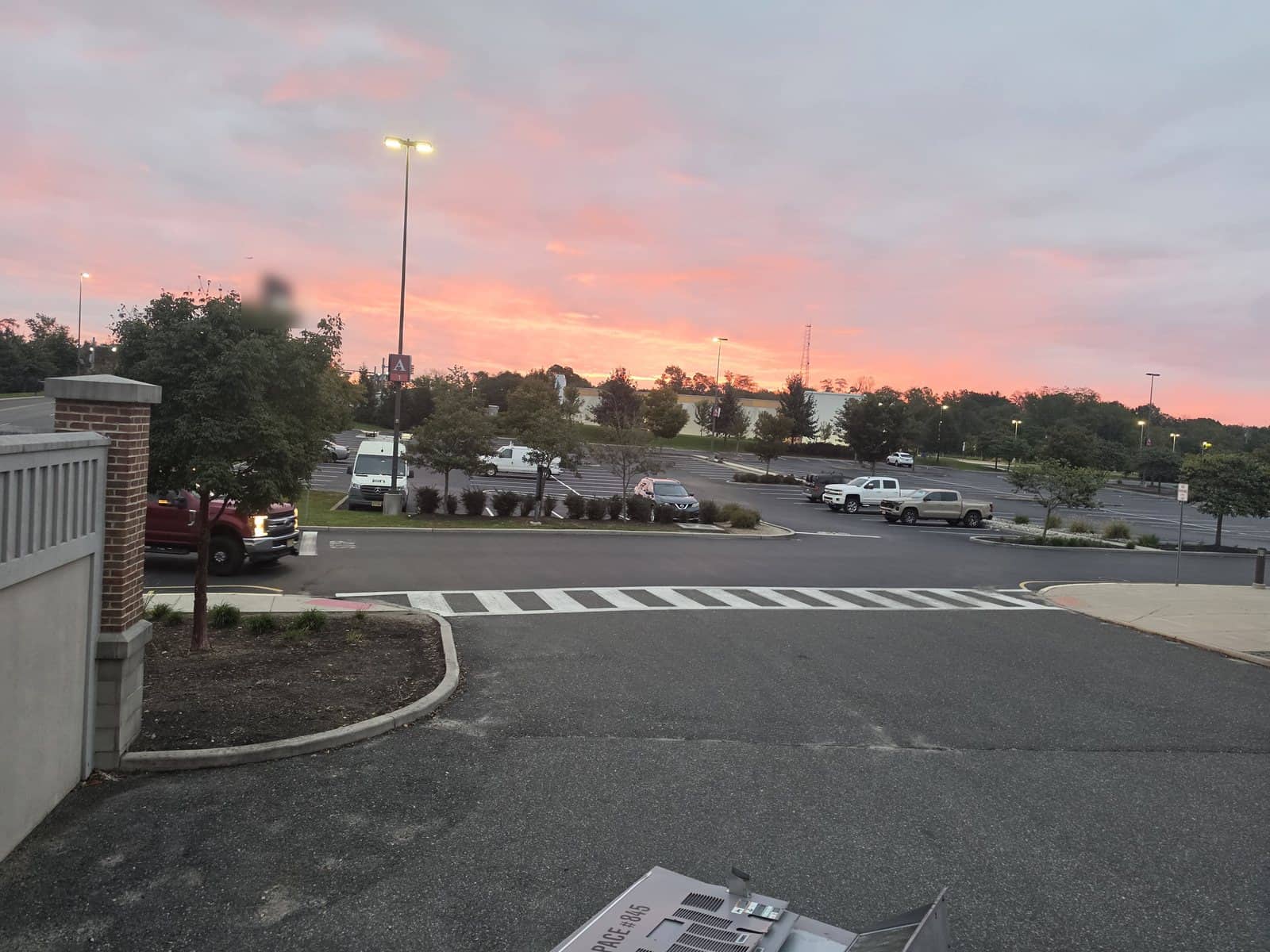 Pink sunrise sky over a shopping center parking lot in Gloucester Township, NJ with an RTU curb piece in the foreground