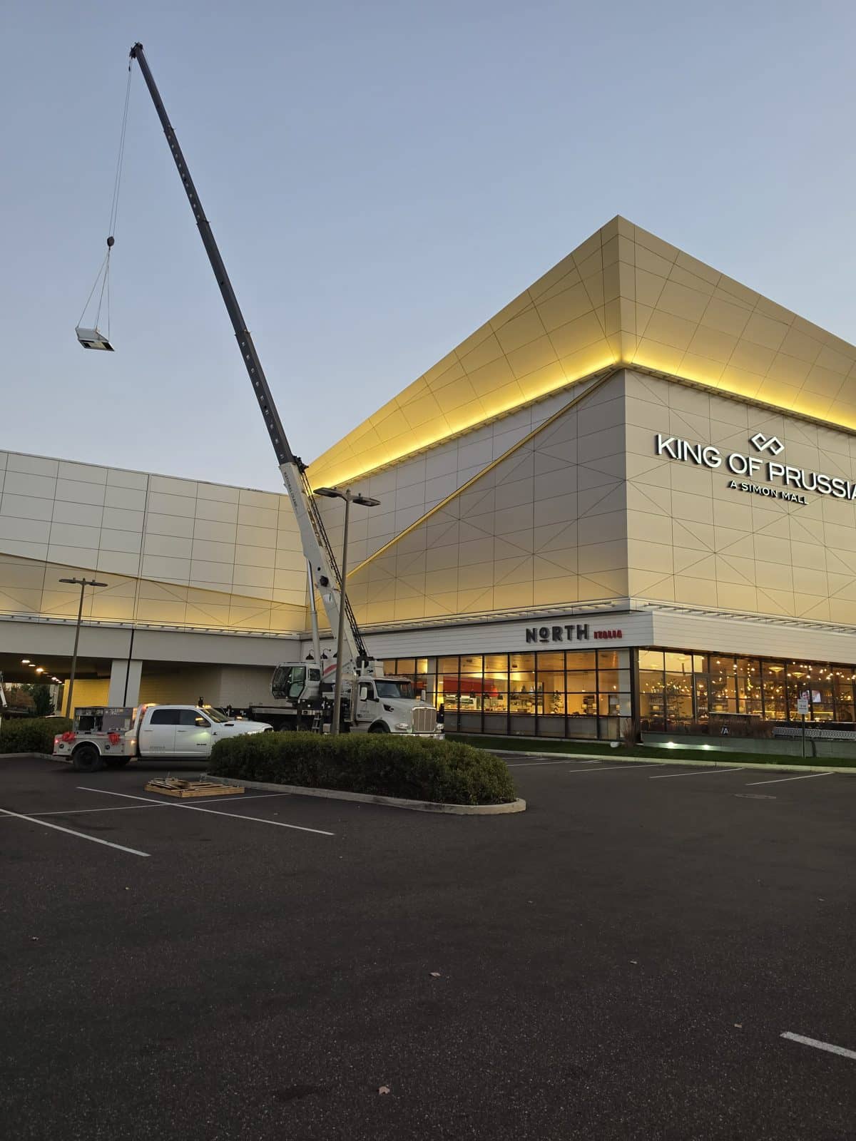 Steedle truck crane lifting a rooftop HVAC unit at dawn in front of the King of Prussia mall facade in King of Prussia, PA
