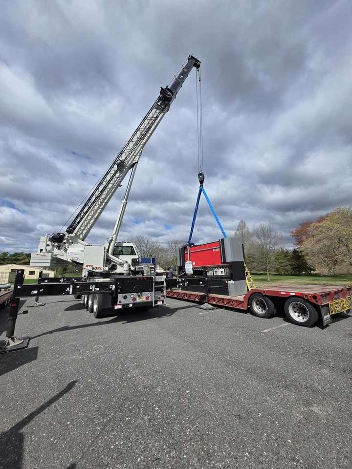 Industrial machinery lifted from a flatbed by truck crane