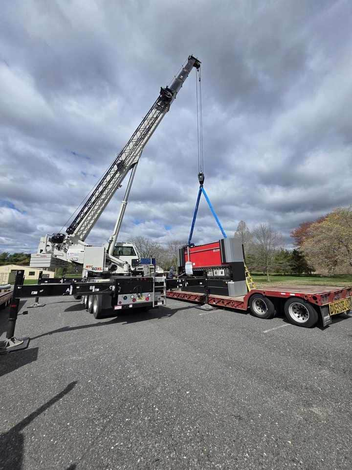 Steedle crane lifting industrial machinery from a flatbed trailer